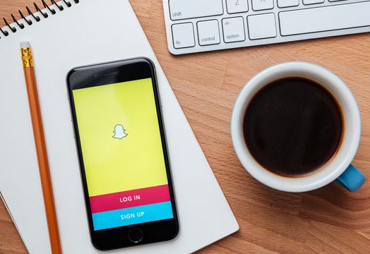 Snapchat on a phone on desk with cup of coffee and pad and keyboard