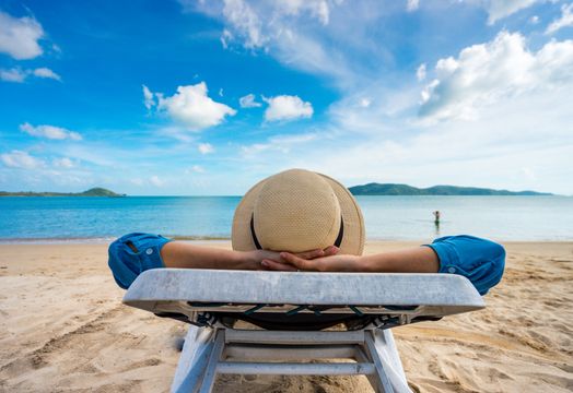 Man wearing a hat relaxing on a sunlounger on a tropical beach